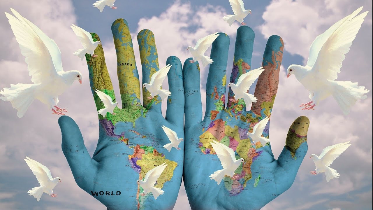 Two hands painted with a world map are held open against a cloudy sky, surrounded by white doves in flight, symbolizing global peace and unity.